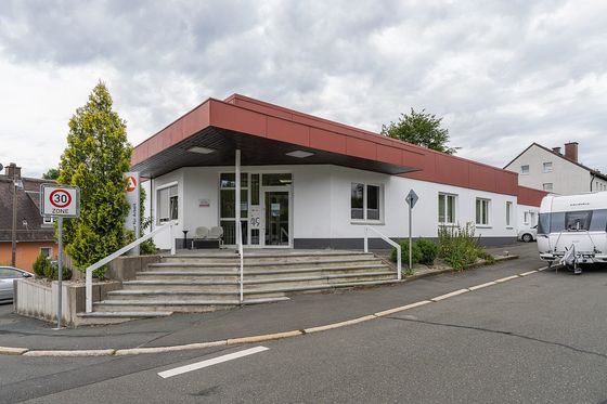 Flaches Gebäude der Agentur für Arbeit mit rotem Dachrand, Treppe und Eingangsschild