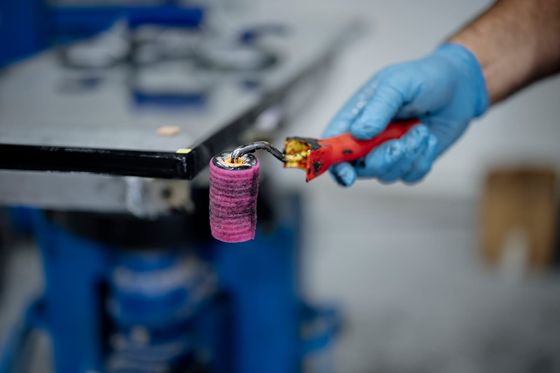 Hand im blauen Handschuh hält eine gebrauchte Farbrolle in einer Werkstatt
