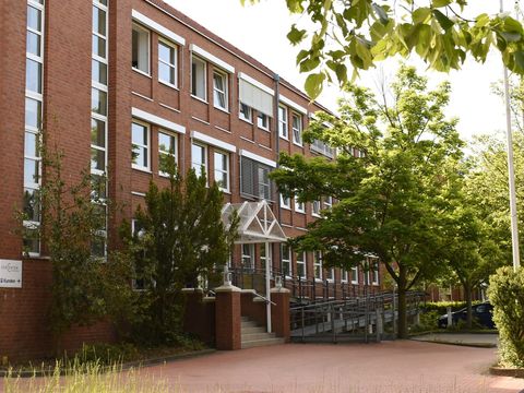 Backsteingebäude eines Jobcenters mit Eingangsrampe und Kundenschild unter grünen Bäumen