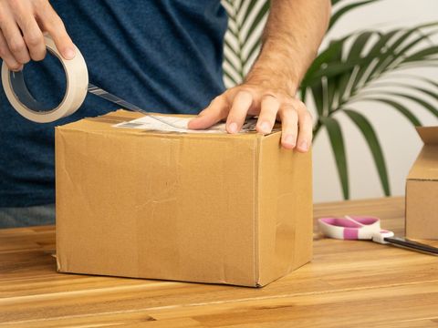 Hände kleben ein Versandetikett mit Klebeband auf einen Karton am Holztisch