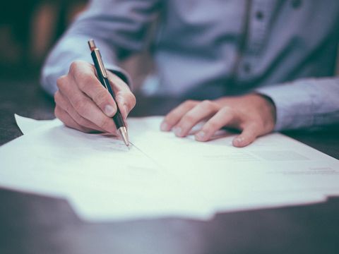 Hand unterschreibt mit Kugelschreiber ein Dokument auf einem dunklen Tisch