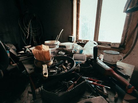 Volle Werkbank mit Werkzeugen, Schrauben und Eimern vor einem hellen Werkstattfenster
