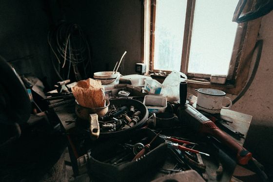 Volle Werkbank mit Werkzeugen, Schrauben und Eimern vor einem hellen Werkstattfenster