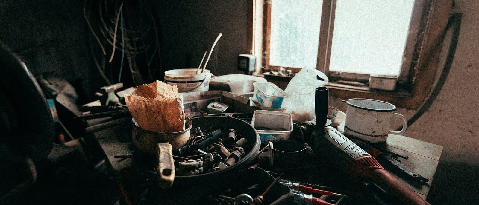 Volle Werkbank mit Werkzeugen, Schrauben und Eimern vor einem hellen Werkstattfenster